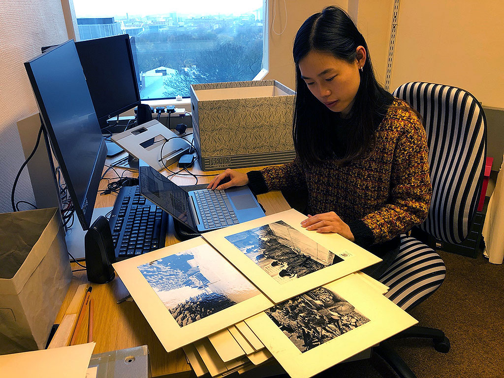 Photo of the cataloguer, Karin, at her desk with photos.