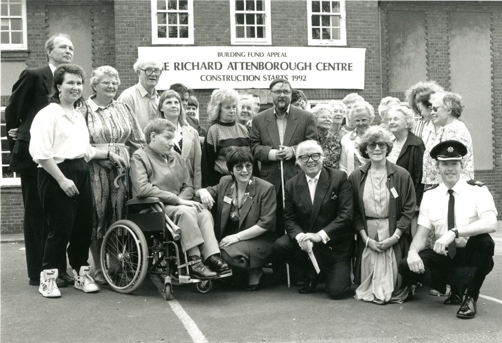 Fundraising appeal for the Richard Attenborough Centre; Richard Attenborough is in the centre of the picture surrounded by others, including people with visual impairments or physical disabilities. 