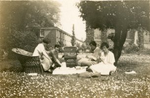 Slightly blurred black and white photograph of a group of students having tea on the University College lawn.