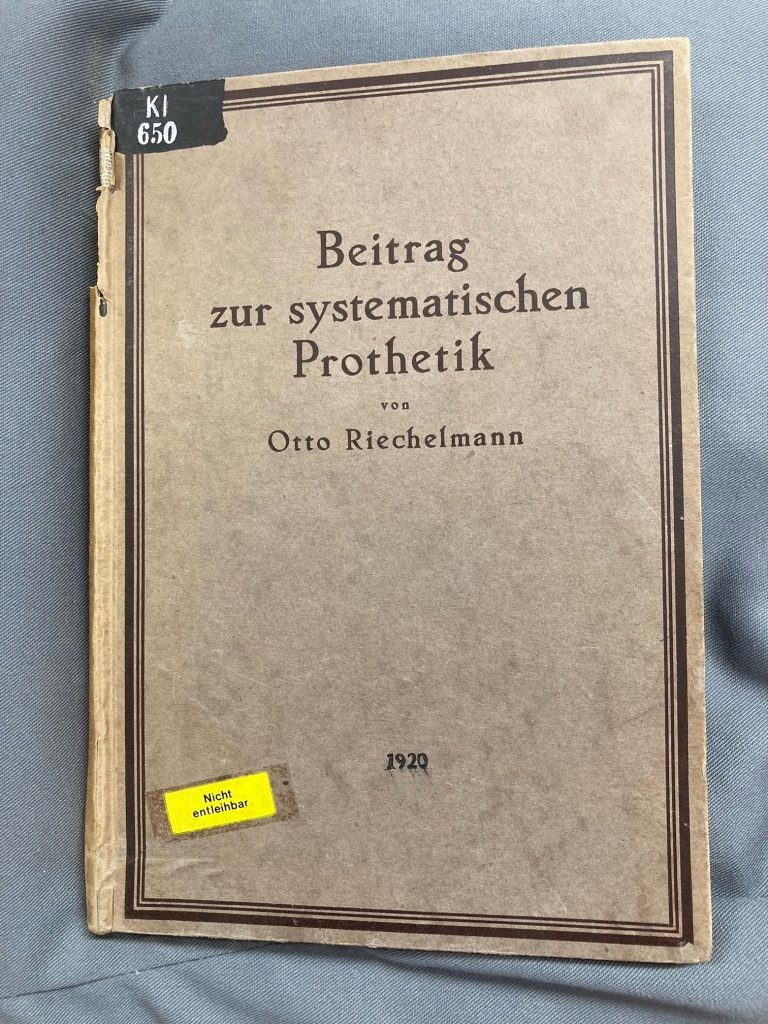 Colour photograph showing the front cover of a German-language dentistry book titled 'Beitrag zur systematischen Prothetik' by Otto Riechelmann, dated 1920