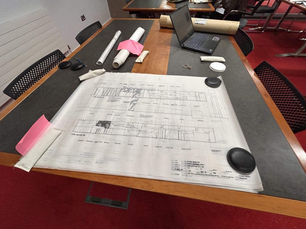 Large plan held open on a desk with small weights